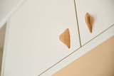Gros plan sur poignées en bois sculpté fixées sur des portes de placard blanc, ajoutant une touche naturelle et élégante.