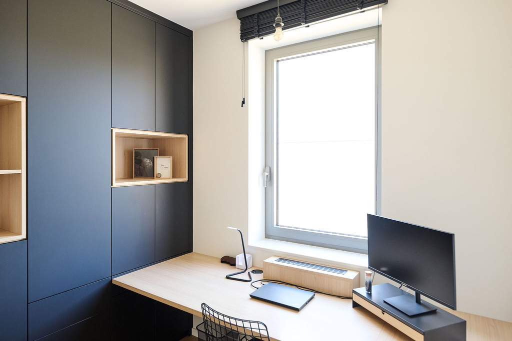 Maatwerk bureau met zwarte kasten, decoratieve nis in licht hout en ruim werkblad onder een raam