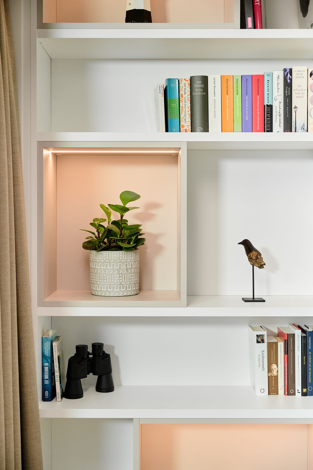 Op maat gemaakte kast met verlichte niche, plant en decoratief object in een moderne woonkamer.