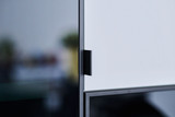 Détail d’une poignée minimaliste sur une porte coulissante en verre et panneau blanc.