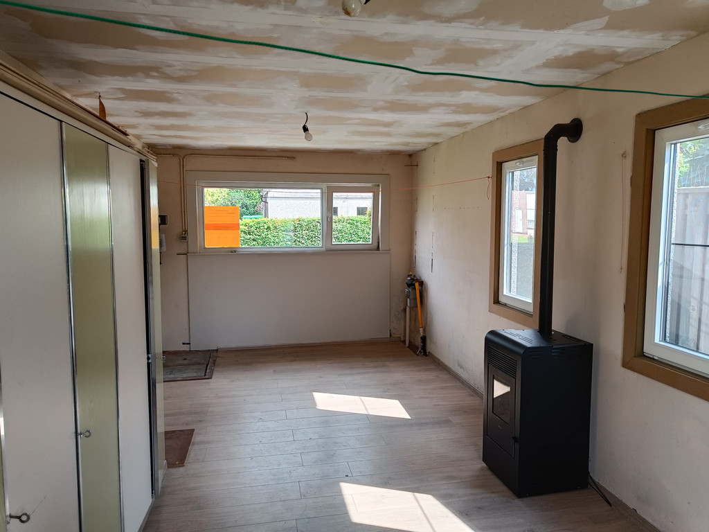Onafgewerkte ruimte met gaskachel oude kasten en zicht op ramen en tuin vóór renovatie met maatwerk