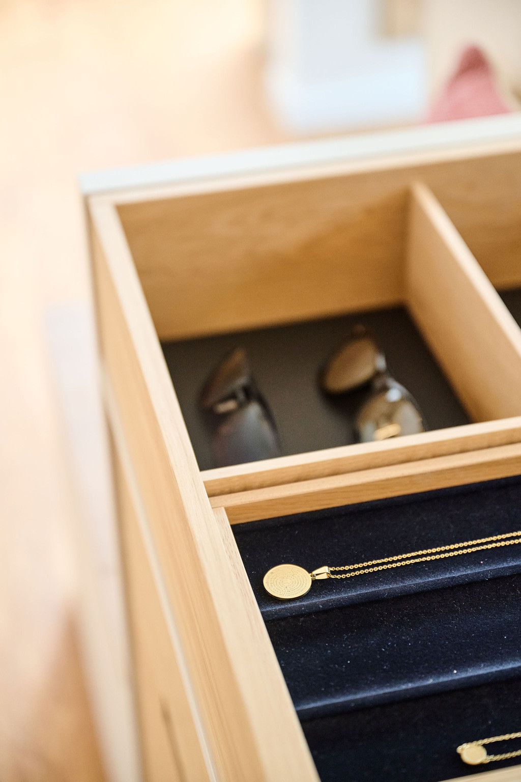 Gros plan d'un tiroir en bois avec compartiments pour lunettes et bijoux, doté d'un fond en velours noir et d'une médaille en or.