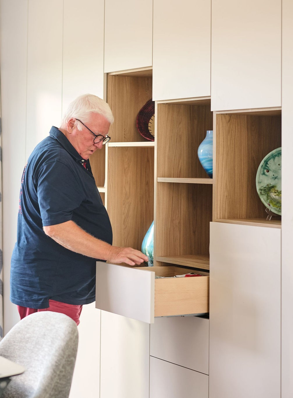 Guido opent een lade van een wandkast op maat met witte fronten en open houten nissen voor decoratie