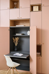 Op maat gemaakt inklapbaar bureau in een roze kast, met open deuren, ingebouwde legplanken en decoratieve accessoires.