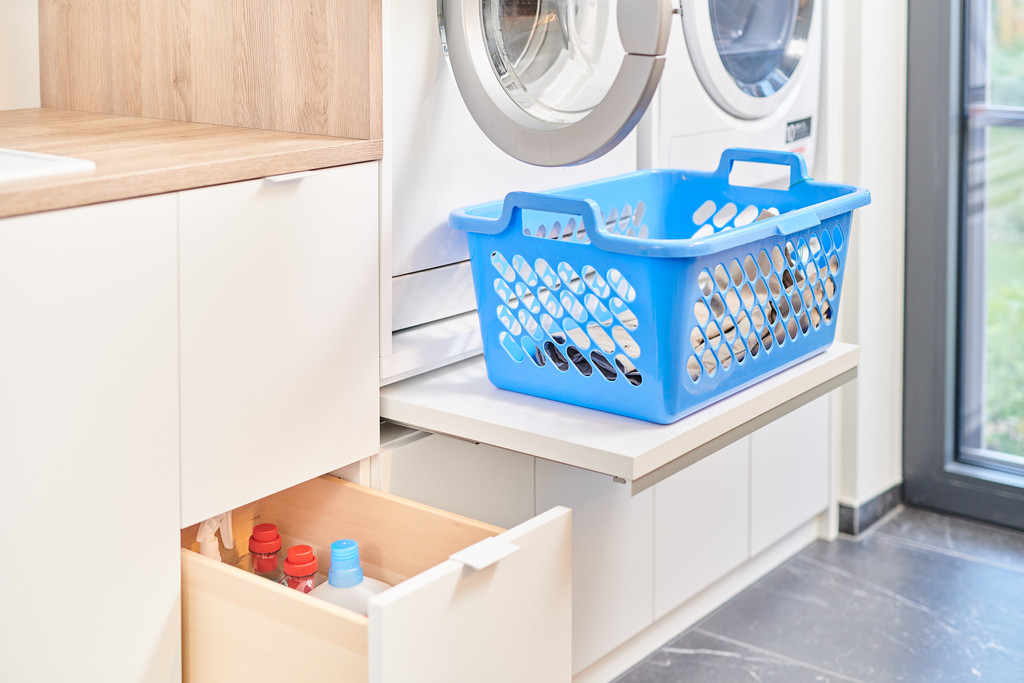Panier bleu de linge posé sur une étagère près d'une machine à laver et d'un tiroir de rangement dans une buanderie.