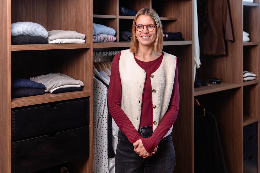 Femme souriante posant devant un dressing sur mesure en bois avec étagères et penderie organisées.