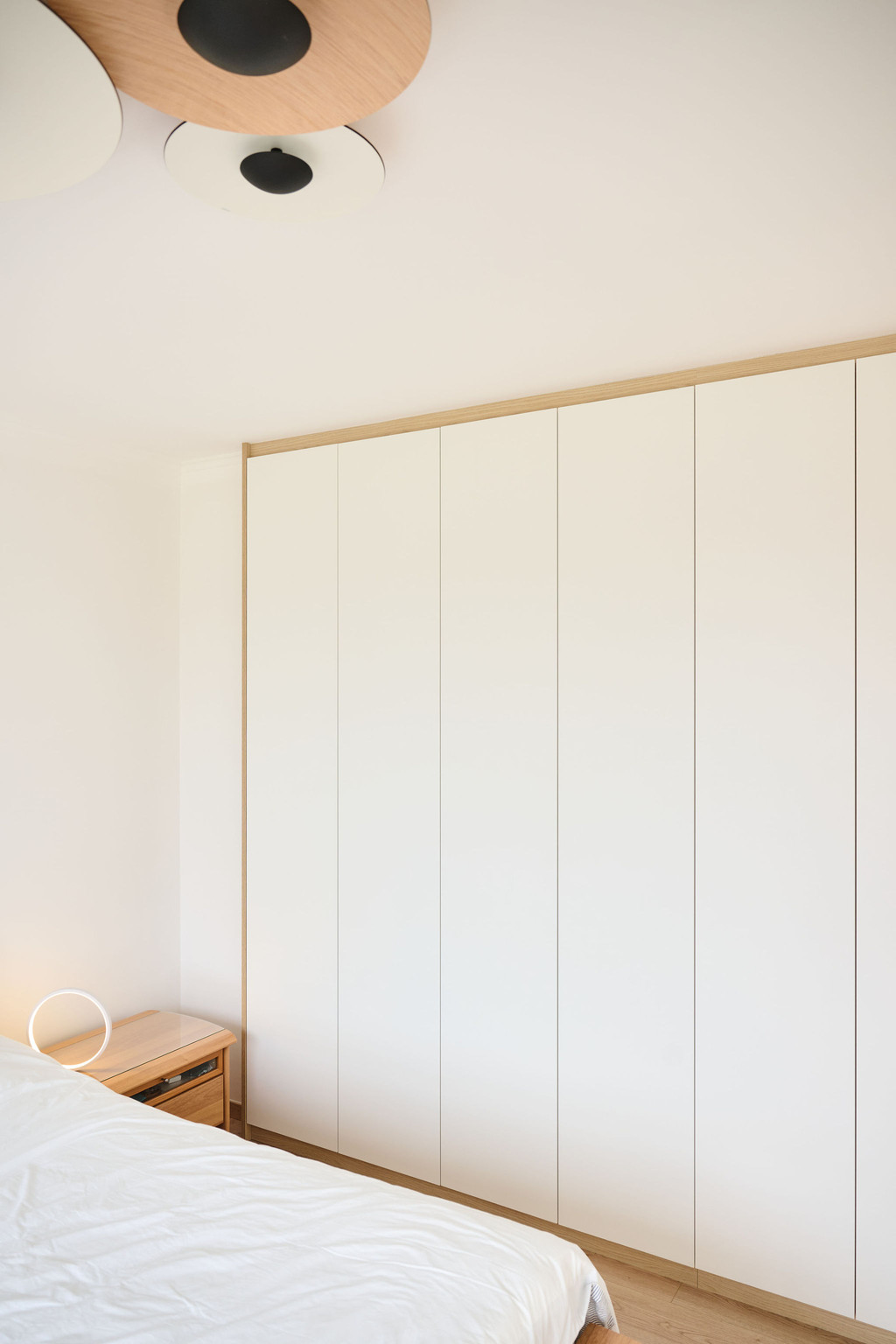 Witte kledingkast op maat van vloer tot plafond in een slaapkamer met greeploze deuren en een subtiele houten omlijsting