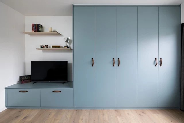 Meuble de rangement sur mesure avec TV et étagères dans une chambre d'enfant, couleur bleu clair avec poignées design.