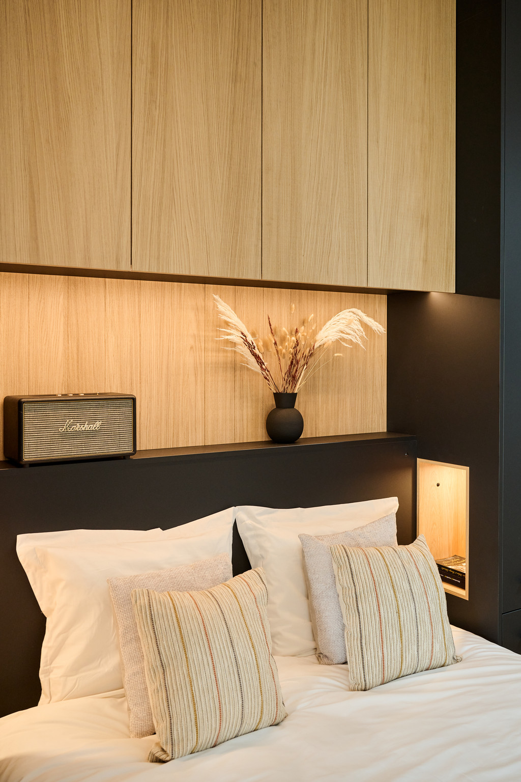 Chambre avec tête de lit sur mesure en bois clair, éclairage intégré et décoration élégante.