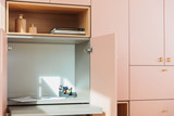 Bureau pliable sur mesure intégré dans un meuble rose, avec étagères ouvertes et accessoires de bureau comme des stylos et des carnets.