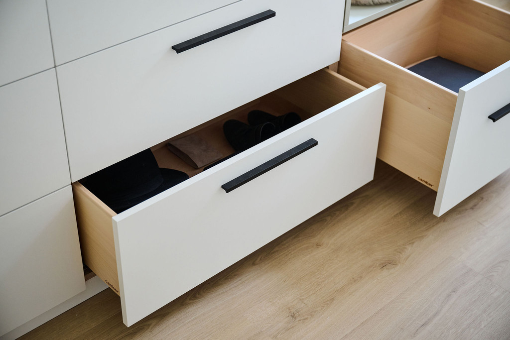 Detail van open witte lades met zwarte grepen en houten interieur in een maatkast op houten vloer