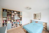 Slaapkamer met wandvullende boekenkast op maat, bed met lichtblauwe bedombouw en geïntegreerde opbergruimte
