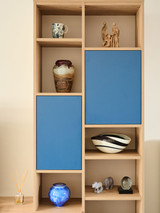 Detail van een houten wandkast op maat met open nissen voor decoratie en gesloten opbergvakken met blauwe fronten
