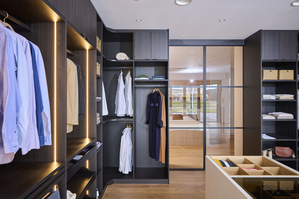 Dressing sur mesure avec penderie, niches ouvertes et éclairage LED intégré en bois foncé dans un showroom
