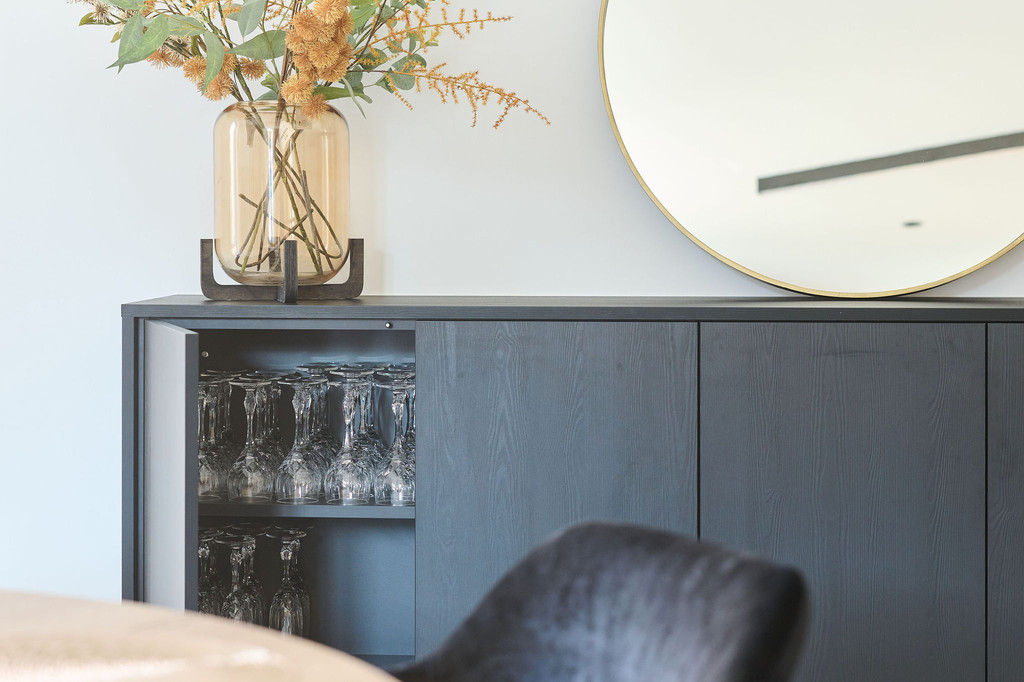 Meuble bas de salon sur mesure avec miroir rond et décoration florale, créant un espace élégant et fonctionnel.