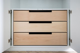 Tiroirs en bois clair sur un meuble de vestiaire fermé sur mesure, avec poignées intégrées pour un accès facile au contenu.