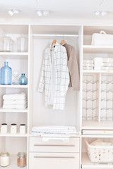 Rangement de buanderie avec étagères ouvertes et penderie pour vêtements, avec des bocaux et des serviettes pliées.