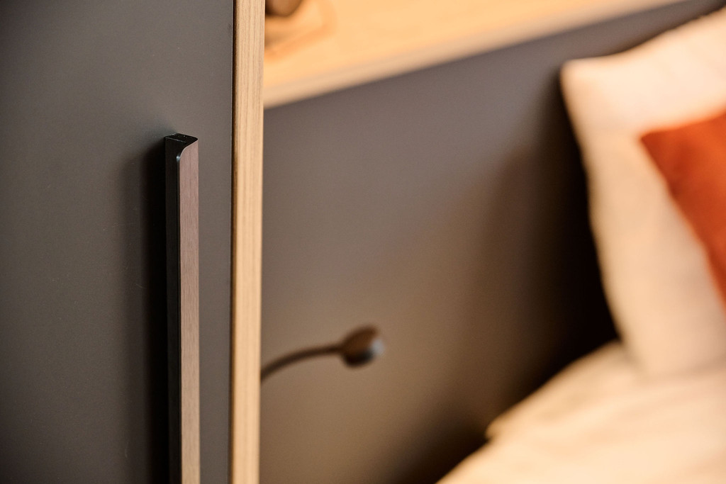 Détail de poignée verticale en métal noir sur meuble sur mesure avec lampe de lecture près du lit