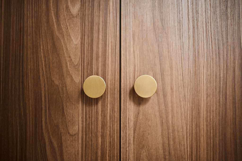 Gros plan sur des portes de placard en bois avec des poignées rondes dorées, apportant une touche élégante et chaleureuse à l’espace.