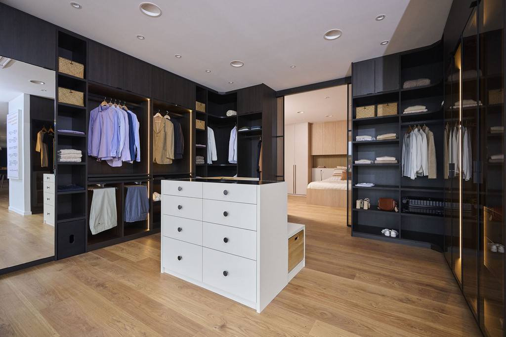 Dressing sur mesure avec îlot central, penderie et niches ouvertes en bois foncé dans un showroom