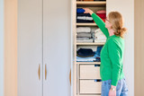 Cliente range ses vêtements dans un placard sur mesure avec étagères et tiroirs dans une chambre lumineuse