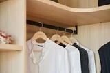 Tringle noire suspendue avec vêtements accrochés dans une penderie en bois sur mesure.