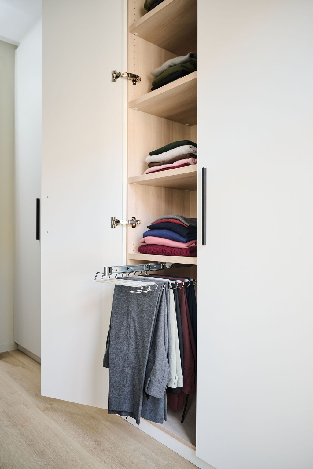 Geopende maatkast met legplanken voor truien en uittrekbare broekhouder in een moderne dressing