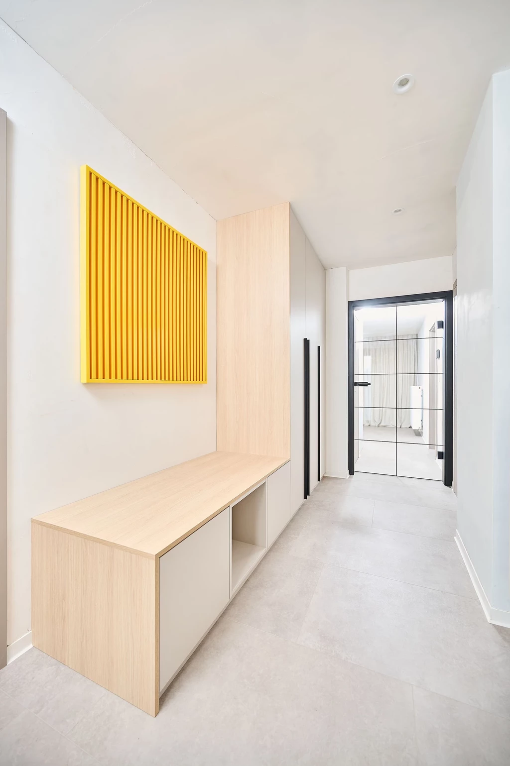 Hall d'entrée avec meuble sur mesure en bois clair, comportant une banquette et un panneau décoratif jaune pour un design moderne.