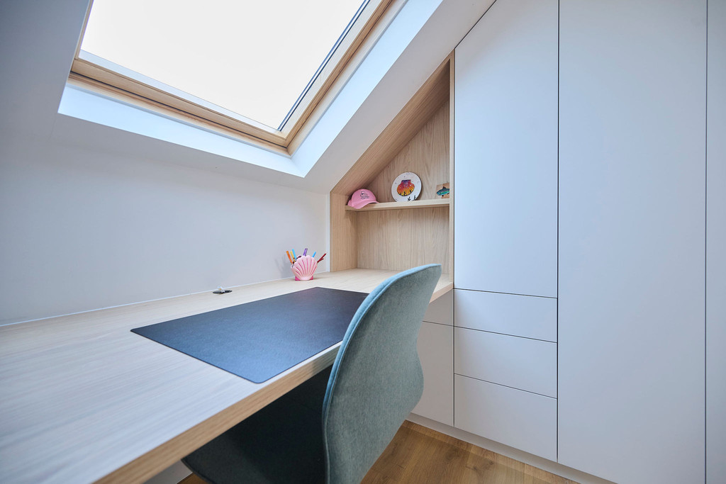 Détail d'un bureau dans une chambre d'enfant sous pente avec étagères et fauteuil confortable.