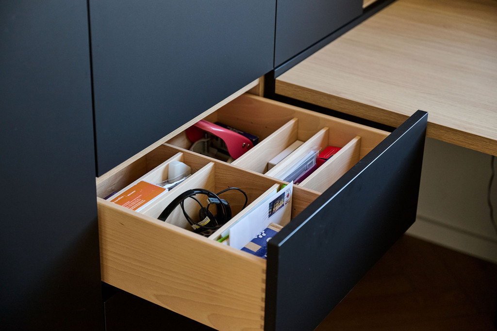 Open zwarte lade met houten indeling voor bureaubenodigdheden zoals kabels, kaarten en nietmachine