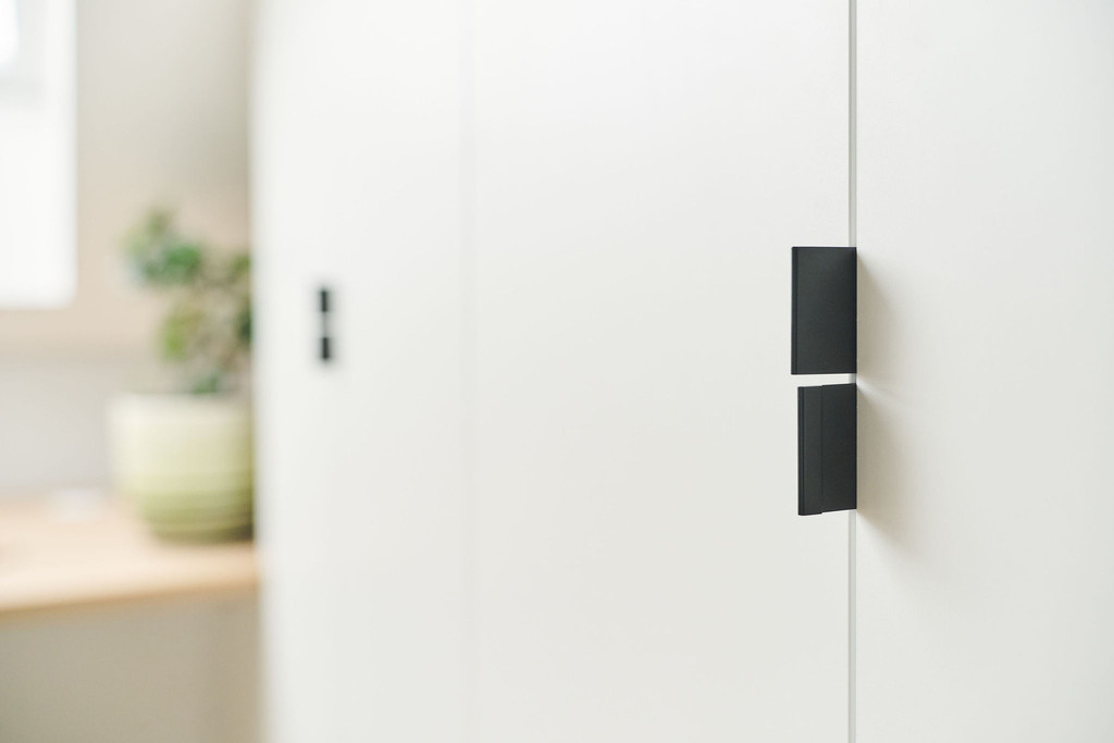 Detail van een witte maatkast onder een schuine wand met moderne zwarte handgrepen, minimalistisch ontwerp met subtiele schaduwen.