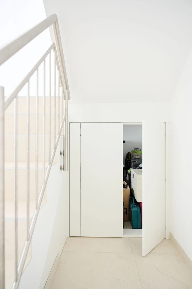 Ingebouwde kast onder een trap met schuine wanden, zichtbaar met opbergruimte achter de deuren.