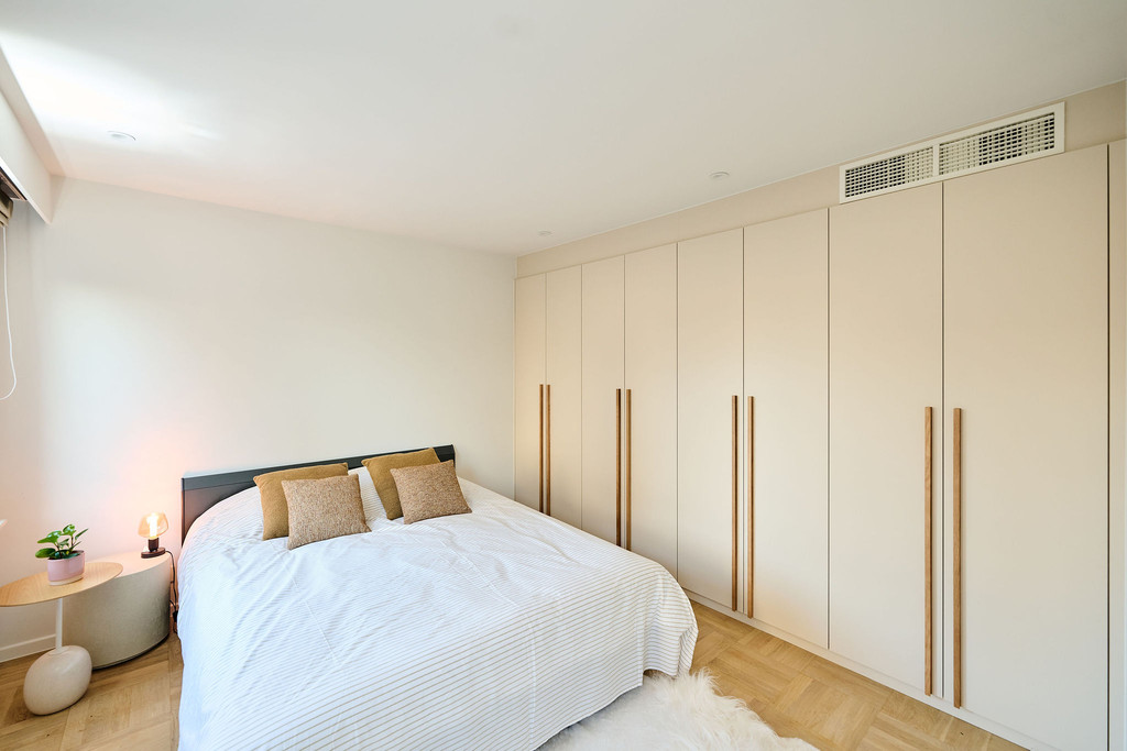 Chambre avec placards blancs sur mesure couvrant tout un mur, longues poignées en bois et lit double avec coussins beiges
