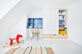 Espace de rangement et bureau intégré pour chambre d'enfant, avec niches bleues et tiroirs en bois clair sous pente.