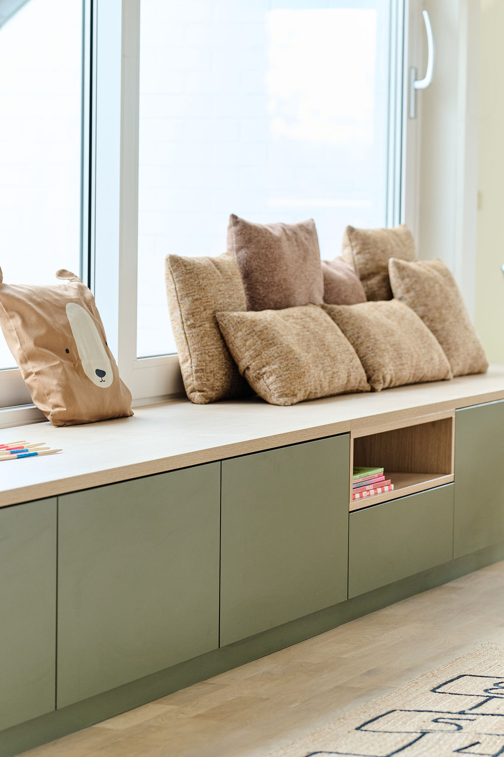 Banquette verte sur mesure avec coussins beiges sous une fenêtre et niche de rangement ouverte