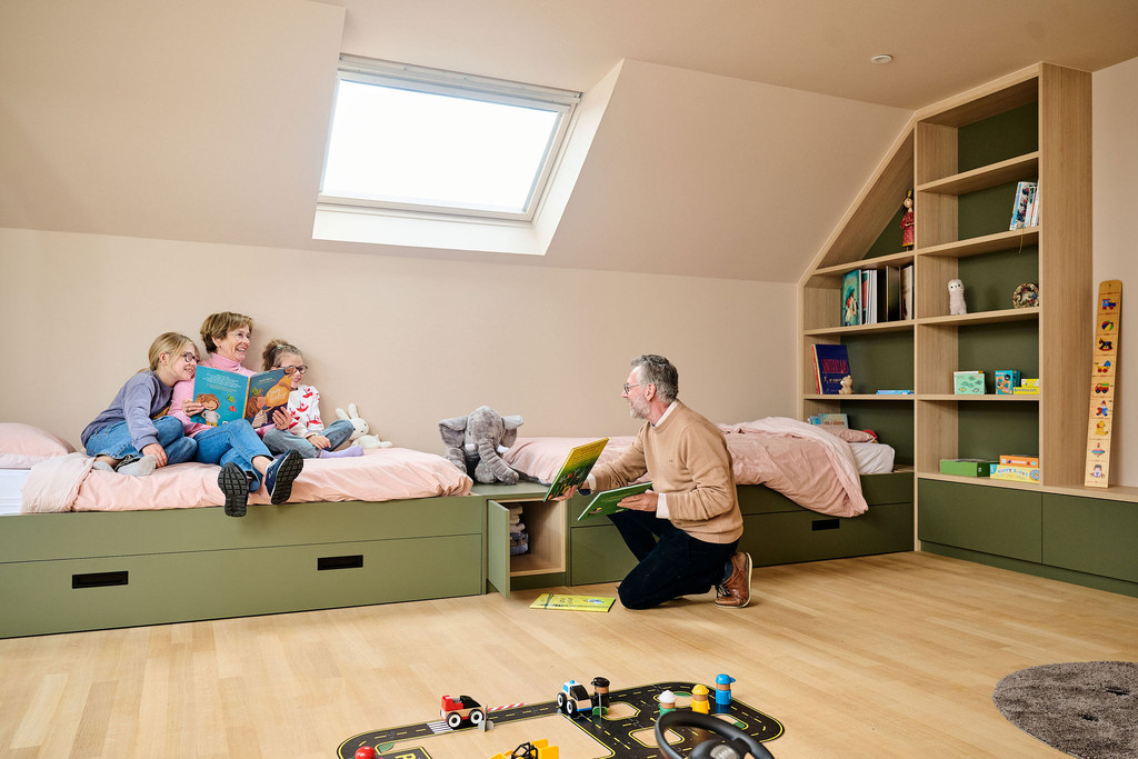 Chambre d’enfants avec deux lits verts sur mesure et rangements intégrés avec parents lisant une histoire aux enfants