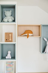 Détail d'étagères avec des figurines et jouets pour enfants, incluant une figurine en bois et un chapeau orange.