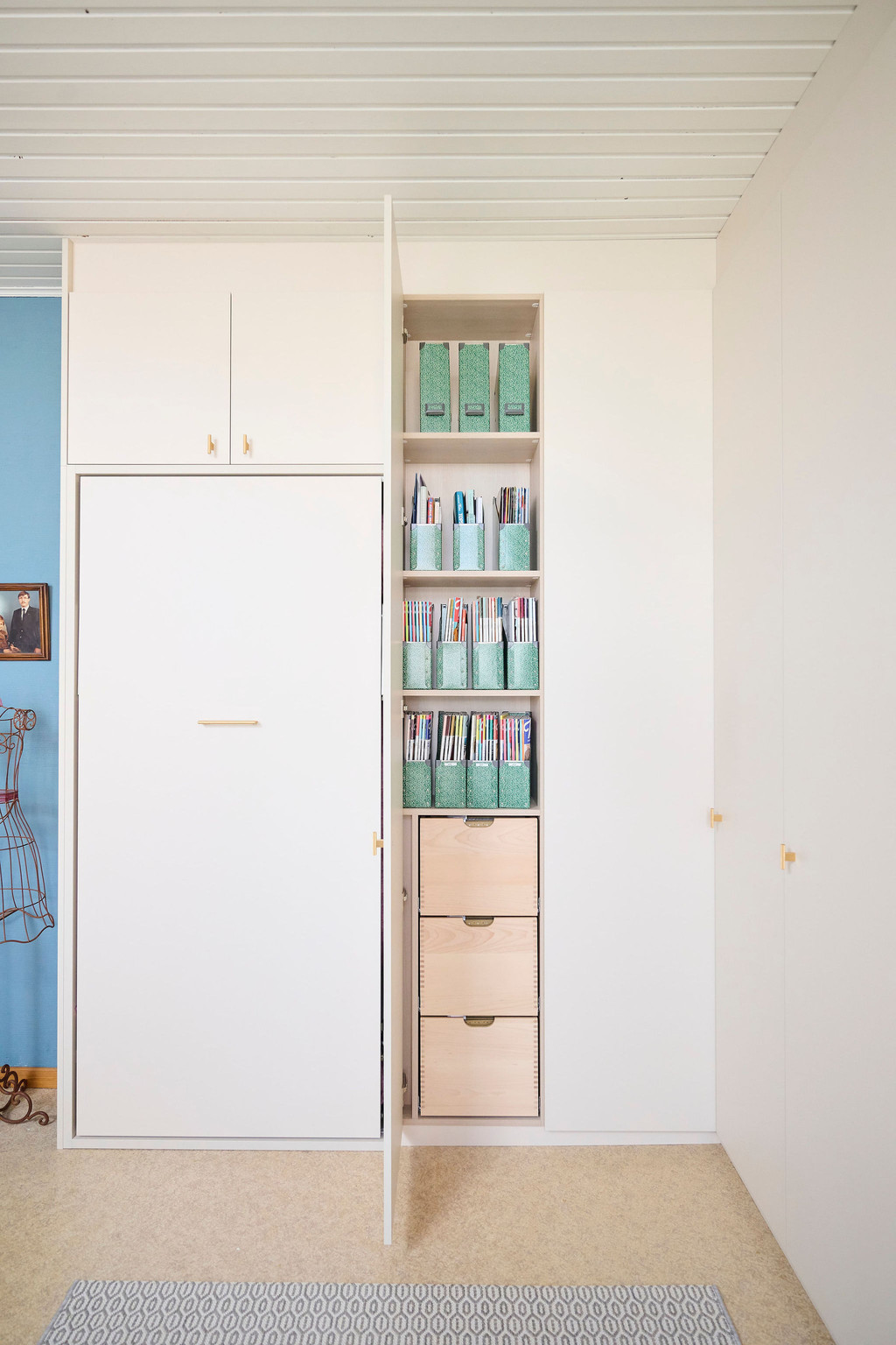 Placard Camber sur mesure pour chambre d’amis avec lit escamotable fermé, niche ouverte pour livres et classeurs et tiroirs en bois intégrés chez Els et Kevin