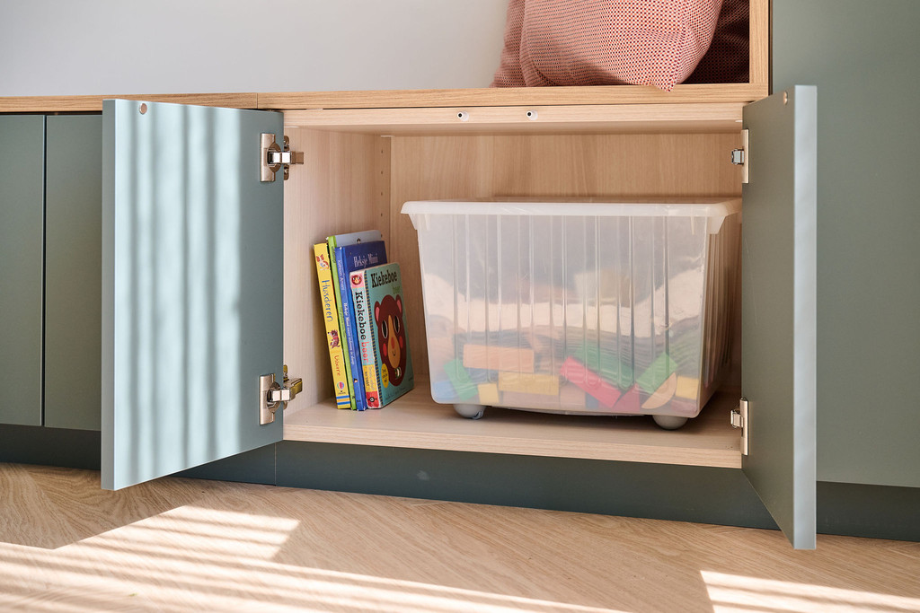Meuble bas sur mesure avec portes ouvertes contenant des livres pour enfants et une boîte de rangement avec jouets