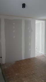 Hall d’entrée vide avec murs en plaques de plâtre non finis et sol carrelé brun avant installation d’une armoire vestiaire
