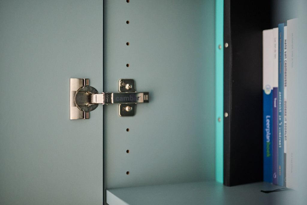Close-up van scharnier in blauw maatwerkkastje met verstelbare legplanken en turquoise boeken