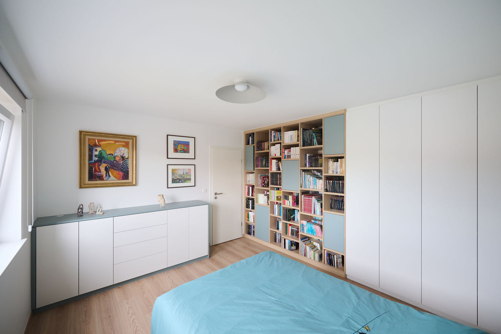 Slaapkamer met wandvullende boekenkast op maat, witte kledingkast en lage opbergkast met lades langs de tegenoverliggende wand