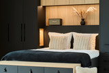 Chambre moderne avec une tête de lit sur mesure noire et bois clair, accompagnée de coussins et d’une lampe.