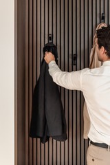 Man hangt een zwarte jas op aan een haak in een op maat gemaakte vestiaire van Camber.