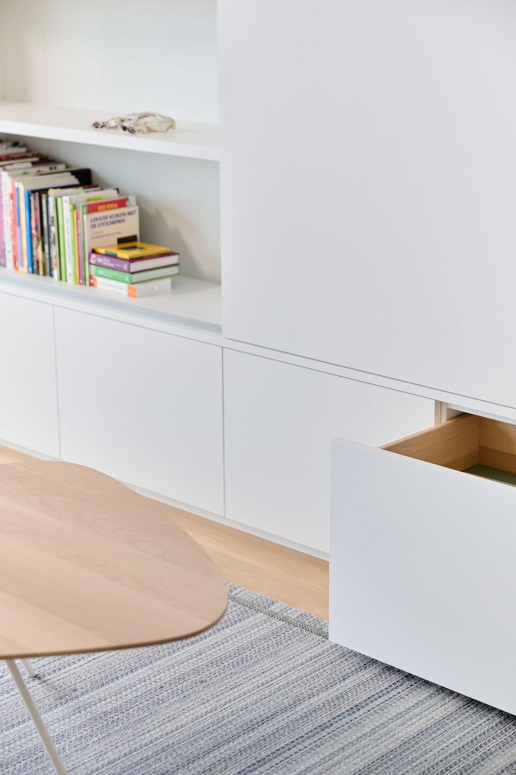 Op maat gemaakte witte kast met open vakken en lades, ingericht met boeken in een moderne woonkamer.