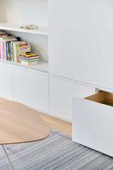 Op maat gemaakte witte kast met open vakken en lades, ingericht met boeken in een moderne woonkamer.