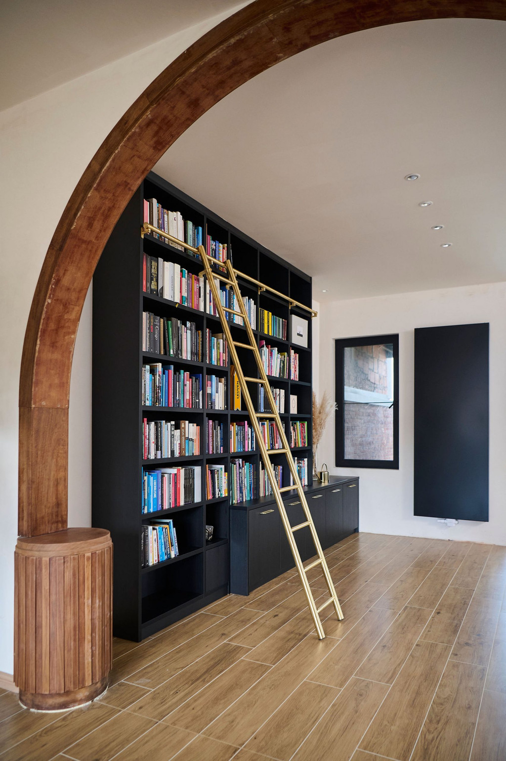 Zwarte boekenkast op maat met open nissen en gouden ladder