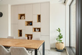 Placard sur mesure avec niches ouvertes en finition bois et rangements fermés, intégré dans une salle à manger lumineuse avec table et plante, réalisé par Camber