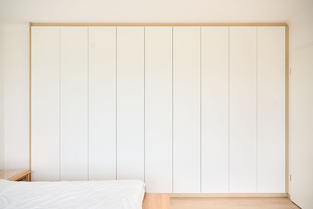 Wandvullende witte kledingkast op maat in een slaapkamer met greeploze deuren en houten afwerking boven- en onderaan