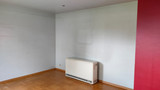 Mur vide avec convecteur dans une pièce au parquet clair et une paroi rouge visible à droite